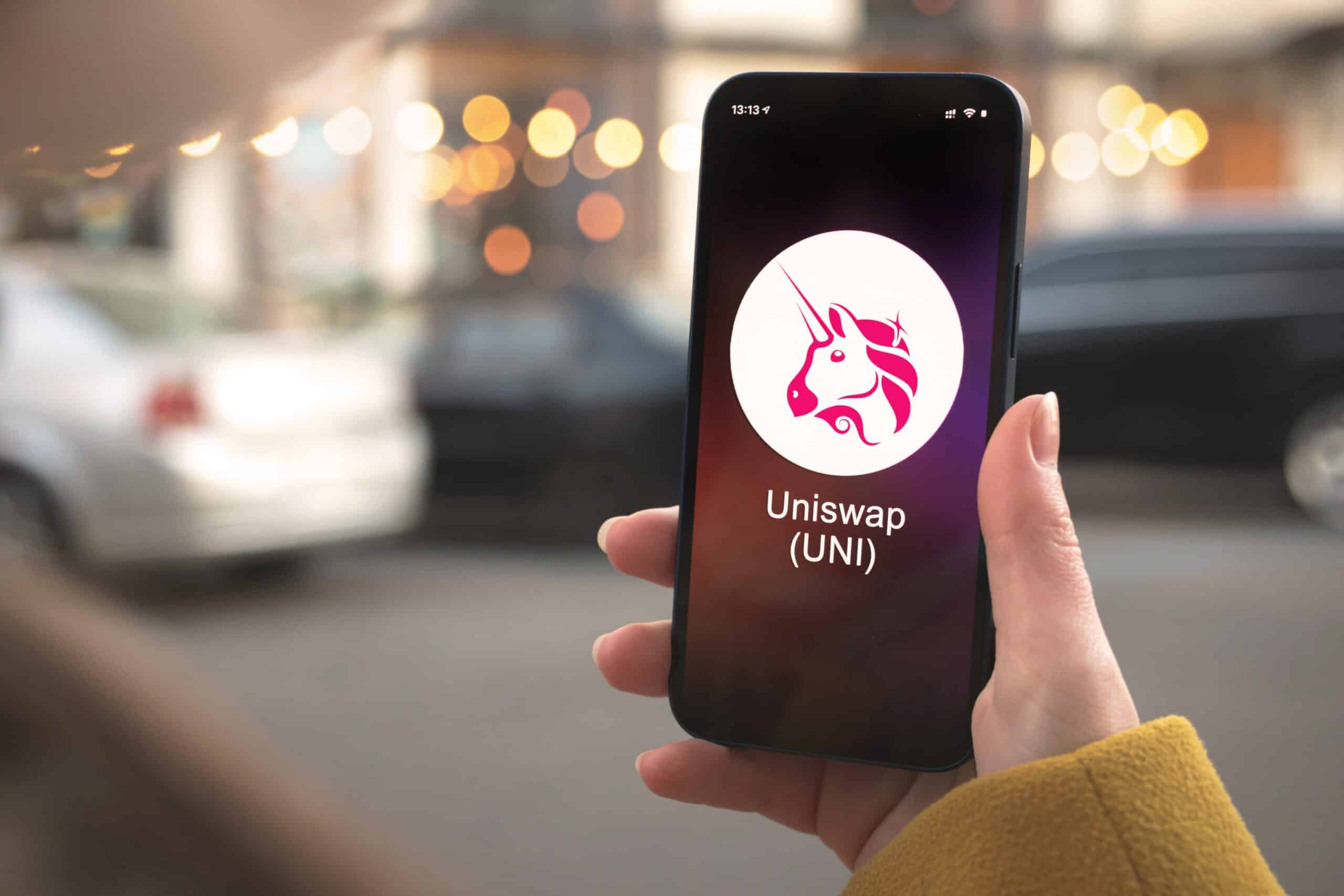 Uniswap's logo of a pink unicorn is displayed on a phone in a person's hand
