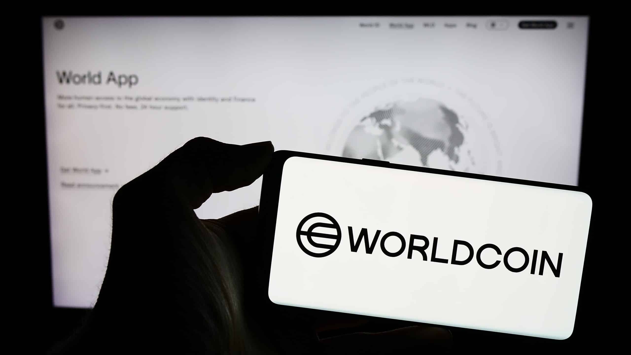A photo of a hand holding a phone displaying "Worldcoin" and its logo. (Shutterstock/T. Schneider)