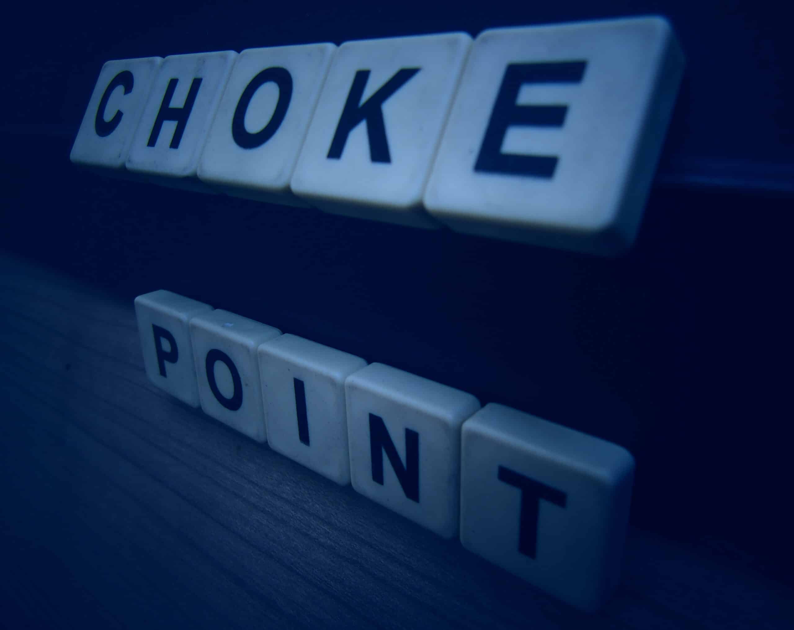 Scrabble letters spell out "Choke Point" on an angle in cool, dim lighting.